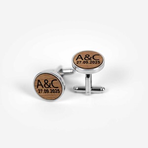 May include: A pair of cufflinks with a wooden face and silver-colored metal backing. The wooden face of each cufflink has the initials "A&C" and the date "27.09.2025" engraved in black. The cufflinks are designed for formal wear.