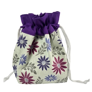 May include: A drawstring bag with a floral pattern. The bag features a cream-colored background with purple, blue, and maroon flowers and gray leaves. The top of the bag is purple, and it has a white drawstring.