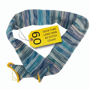 May include: A knitted sock tube in shades of blue and teal with a yellow tag. The tag reads "SOCK TUBE LANG YARN 60 STITCH COUNT" and the number "60" is prominently displayed. The ends of the tube have yellow trim.