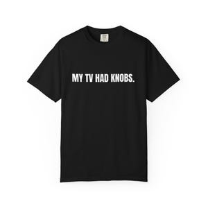 May include: A black short-sleeve t-shirt featuring the white text MY TV HAD KNOBS. printed in a clean, sans-serif font across the center of the chest. The garment has a standard crew neckline and a label visible at the inner back collar area.