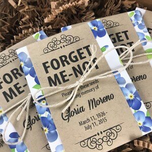 以下が含まれることがあります： 青いワスレナグサの花と「Forget Me Not」と「Gloria Moreno」の文字、そして1926年3月11日～2015年7月11日の日付が書かれた茶色の紙袋。