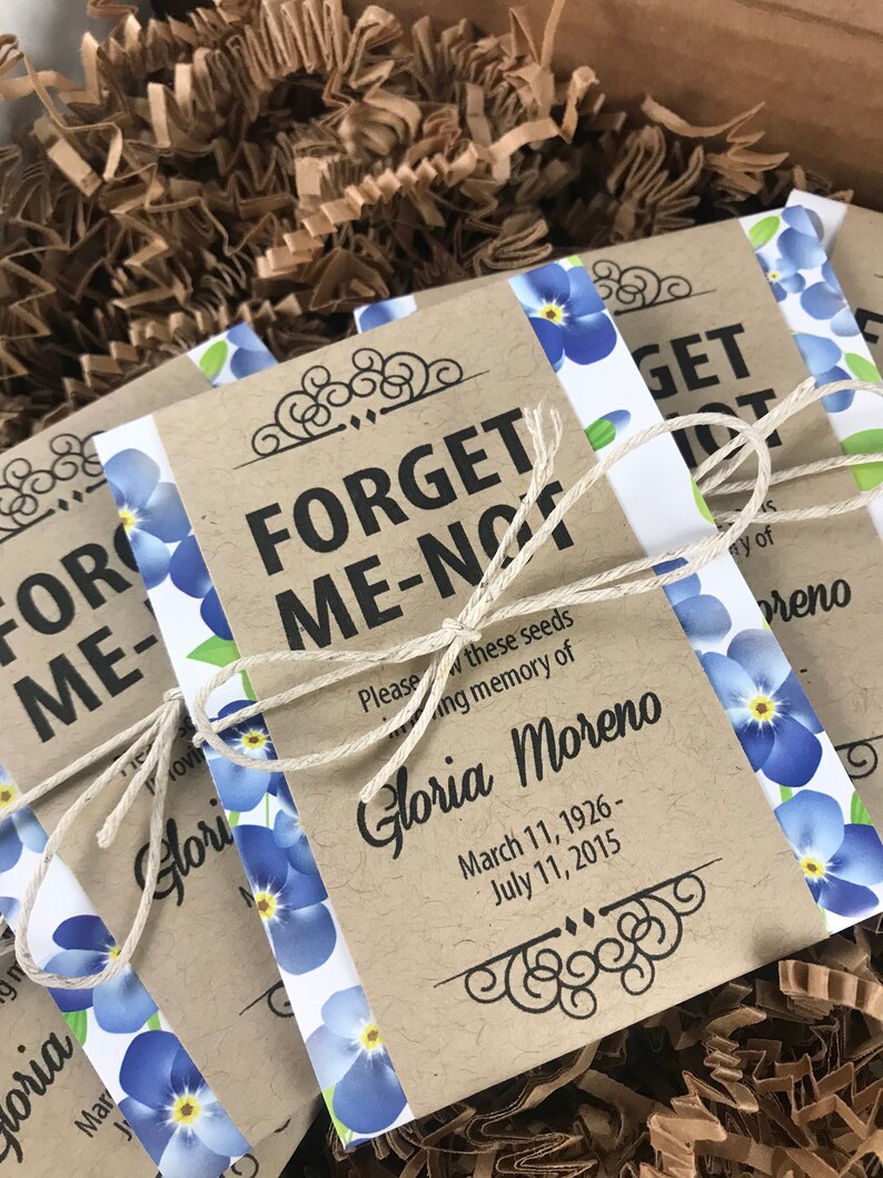 以下が含まれることがあります： 青いワスレナグサの花と「Forget Me Not」と「Gloria Moreno」の文字、そして1926年3月11日～2015年7月11日の日付が書かれた茶色の紙袋。