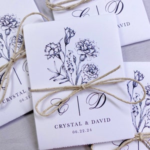 May include: White wedding favor bags with a black floral design and the names Crystal and David, tied with twine.