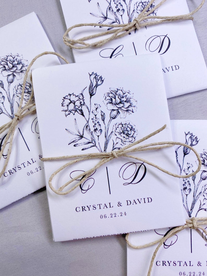 May include: White wedding favor bags with a black floral design and the names Crystal and David, tied with twine.