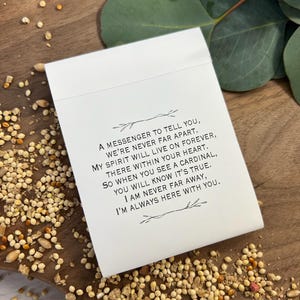 Peut inclure: Une carte blanche avec un message imprim&eacute;, entour&eacute;e de graines pour oiseaux et de verdure. Le texte se lit : &laquo; Un messager pour vous dire, nous ne sommes jamais loin. Mon esprit vivra pour toujours... Je suis toujours l&agrave; avec vous. &raquo;