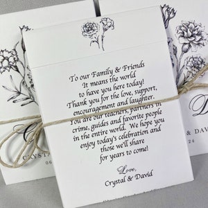 May include: Two white cards with black ink, tied together with twine. The cards feature a floral design and text that reads "To our Family & Friends It means the world to have you here today! Thank you for the love, support, encouragement and laughter. You are our teachers, partners in crime, guides and favorite people in the entire world. We hope you enjoy today's celebration and those we'll share for years to come! Love, Crystal & David"