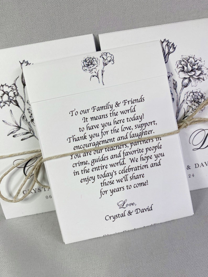 May include: Two white cards with black ink, tied together with twine. The cards feature a floral design and text that reads "To our Family & Friends It means the world to have you here today! Thank you for the love, support, encouragement and laughter. You are our teachers, partners in crime, guides and favorite people in the entire world. We hope you enjoy today's celebration and those we'll share for years to come! Love, Crystal & David"