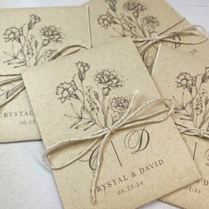May include: A set of brown paper envelopes with a floral design and the text "Crystal & David 06.22.24" printed on the front. The envelopes are tied with twine.