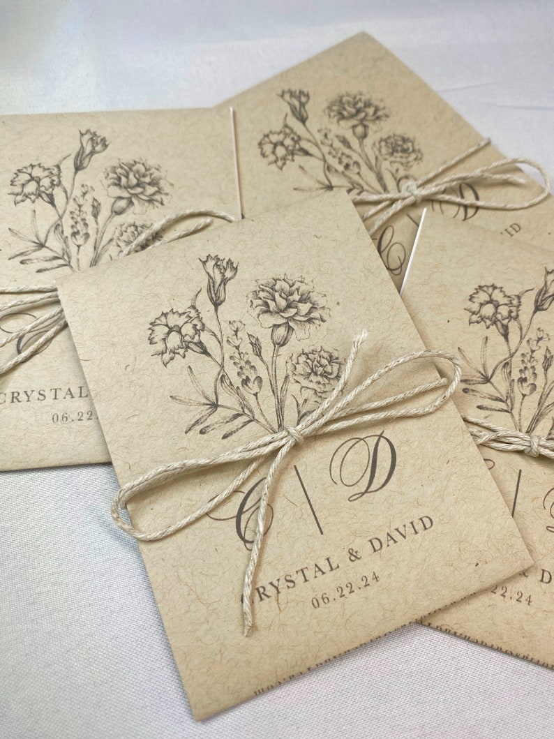 May include: A set of brown paper envelopes with a floral design and the text "Crystal & David 06.22.24" printed on the front. The envelopes are tied with twine.