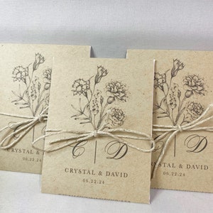 May include: Three kraft paper envelopes with a floral design and the text "Crystal & David 06.22.24" tied with twine.