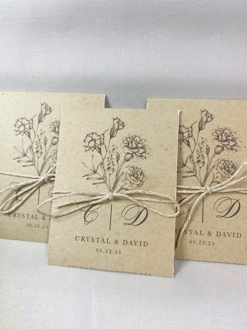 May include: Three kraft paper envelopes with a floral design and the text "Crystal & David 06.22.24" tied with twine.