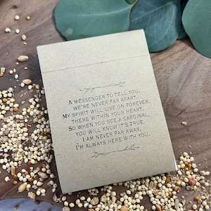 Peut inclure: Une petite carte rectangulaire beige avec du texte noir, entour&eacute;e de graines pour oiseaux et de feuilles d'eucalyptus. Le texte dit : "Un messager pour vous dire, nous ne sommes jamais loin."