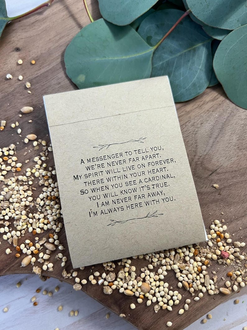 Peut inclure: Une petite carte rectangulaire beige avec du texte noir, entour&eacute;e de graines pour oiseaux et de feuilles d'eucalyptus. Le texte dit : "Un messager pour vous dire, nous ne sommes jamais loin."