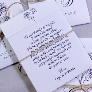 May include: White wedding favor envelopes with a floral design and twine tied around them. The text on the envelope reads "To our Family & Friends It means the world to have you here today! Thank you for the love, support, encouragement and laughter. You are our teachers, partners in crime, guides and favorite people in the entire world. We hope you enjoy today's celebration and those we'll share for years to come! Love, Crystal & David"