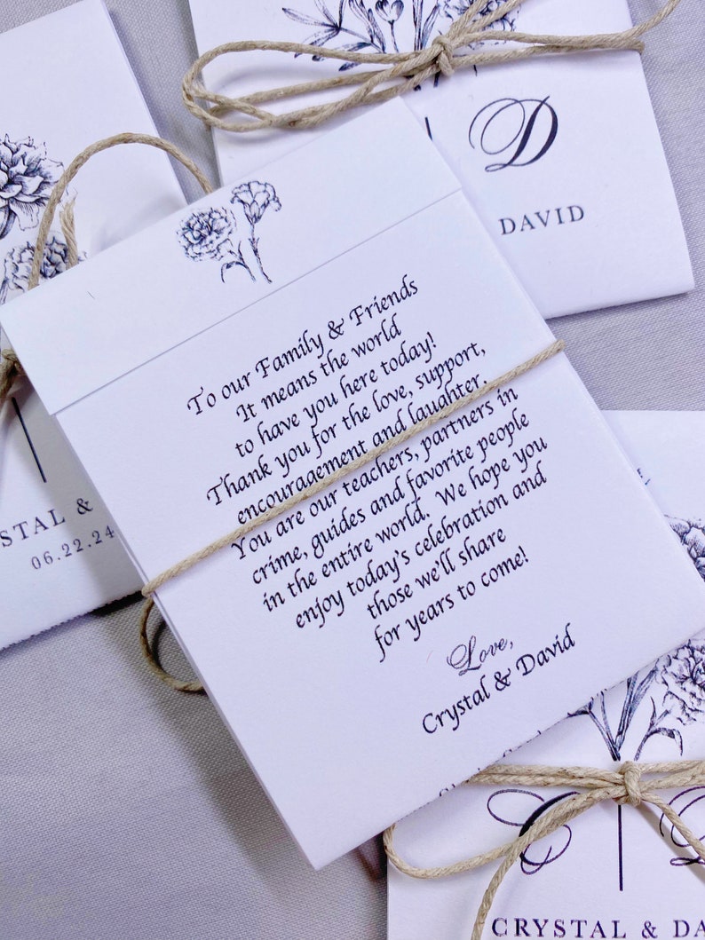 May include: White wedding favor envelopes with a floral design and twine tied around them. The text on the envelope reads "To our Family & Friends It means the world to have you here today! Thank you for the love, support, encouragement and laughter. You are our teachers, partners in crime, guides and favorite people in the entire world. We hope you enjoy today's celebration and those we'll share for years to come! Love, Crystal & David"