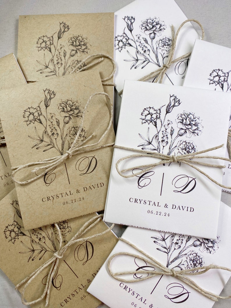 May include: A stack of brown and white paper bags with twine tied around them. Each bag has a floral design and the text "CRYSTAL & DAVID" with a date.