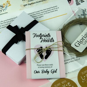 May include: A pink and white memorial seed packet with the text "Footprints on our Hearts" and a pink heart with black footprints. The packet is tied with twine and includes the text "Please sow these seeds in loving memory of Our Baby Girl".