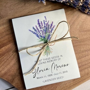 May include: A white seed packet tied with twine, featuring a watercolor illustration of lavender. Text reads "Plant these seeds in loving memory of Gloria Moreno, March 11, 1926 - July 11, 2015, Lavender Seed."