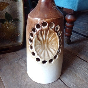 May include: A ceramic bottle with a brown and white glaze. The bottle has a decorative design with a raised, embossed butterfly pattern and a series of holes around the centre.