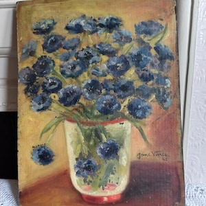 May include: An oil painting on board depicting a bouquet of dark blue flowers in a light-coloured vase with a red rim. The background is a warm yellow and brown tone. The artist signature Jane Vince 42 is visible in the lower right corner of the artwork.