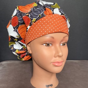 May include: A brown and white patterned scrub hat with a solid orange band. The hat has a pumpkin and leaf design.