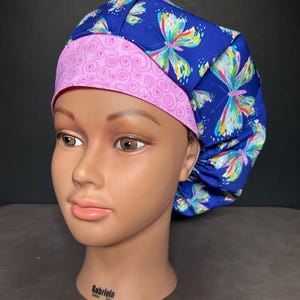 Könnte beinhalten: Eine blaue und rosa chirurgische Mütze mit einem Schmetterlingsmuster. Die Mütze hat ein rosa Innenfutter mit einem Wirbelmuster.