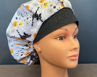 Könnte beinhalten: Eine graue und schwarze Scrubb-Mütze mit Halloween-Motiv. Die Mütze hat ein Muster aus Kürbissen, Fledermäusen, Geistern und Spinnen. Der Text "Boo!" ist auf der Mütze aufgedruckt.