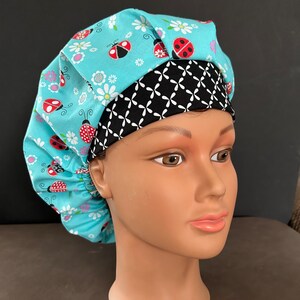 May include: A blue and black scrub hat with a ladybug and daisy print. The hat has a black and white patterned band.