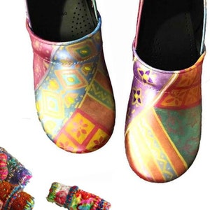 May include: A pair of slip-on clogs featuring a multi-colored geometric pattern in shades of pink, purple, yellow, and teal. The shoes have a rounded toe and a smooth finish. Below the clogs are two small, textured fabric scraps with colorful stitching.