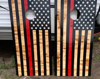 May include: Two wooden cornhole boards with a red stripe and an American flag design. The boards are black with a wood grain pattern and white stars on a blue field.