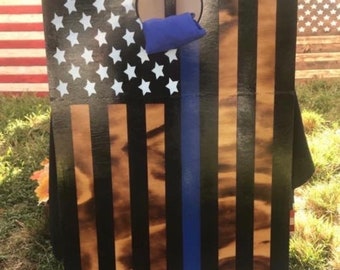 May include: A wooden game board featuring a black and blue American flag design. The board has a hole in the centre and is painted with a thin blue line down the centre.