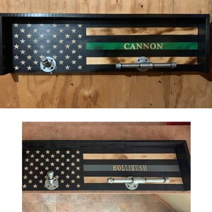May include: A wooden shelf with a black and green American flag design. The shelf has a metal pipe for hanging items and the name "CANNON" is written on the shelf. A second shelf with the same design has the name "HOLLIBUSH" written on it.