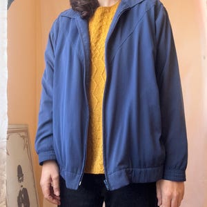 May include: A solid blue zip-up jacket featuring a pointed collar, long sleeves with elastic cuffs, and a matching elastic waistband. The jacket has a front zipper closure and a distinct V-shaped seam detail across the chest area.