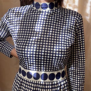 May include: A long-sleeved dress featuring a high mock neck and a waist band, both decorated with large dark blue polka dots on a cream background. The main body of the dress is covered in a dense pattern of smaller dark blue polka dots on cream.