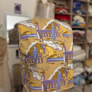 May include: A sleeveless top with a repeating pattern of figures in dresses and hats, set against a landscape of yellow, purple, and white. The top is displayed on a mannequin. The overall color palette is muted, with a vintage aesthetic.
