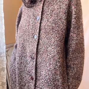 May include: A long-sleeved, collarless jacket made of a textured, multi-coloured tweed fabric in shades of brown, black, and muted red. The jacket features a front button closure with four dark, round buttons and two side pockets.