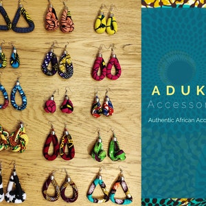 Könnte beinhalten: Eine Sammlung von bunten Stoffohrringen mit verschiedenen Mustern und Formen, darunter Dreiecke, Ovale und Knoten. Die Ohrringe werden auf einer Holzoberfläche präsentiert. Der Text "ADUKU Accessories Authentic African Accessories" ist im Hintergrund sichtbar.