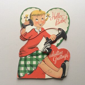 May include: A vintage Valentine's Day card featuring a cartoon girl with pigtails holding a rotary phone. The card is shaped like a heart and has the text "Hello Babe!" and "Valentine Greetings!" on it.