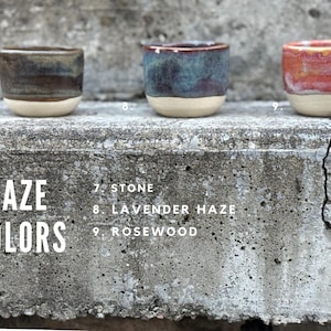 K&ouml;nnte beinhalten: Drei kleine Keramikbecher mit unterschiedlichen Glasuren. Becher 7 ist Stone, eine Mischung aus Dunkelbraun und Grau. Becher 8 ist Lavender Haze mit Blau- und Violettt&ouml;nen. Becher 9 ist Rosewood mit leuchtenden Rot- und Oranget&ouml;nen. Alle haben einen cremefarbenen Boden.