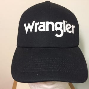 May include: Black baseball cap with the white word "Wrangler" across the front. The cap has a curved brim and a mesh back. The hat is made of a durable fabric.