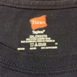 May include: A navy blue t-shirt with a Hanes Tagless&reg; label. The label indicates the shirt is size 2XL and is made of 100% cotton. The shirt is made in Honduras.