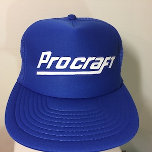 May include: A royal blue trucker hat with a white mesh back and a white "ProCraft" logo embroidered on the front.