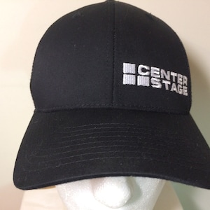 May include: Black mesh trucker hat with a white embroidered logo that says "CENTER STAGE" with a graphic of four squares.