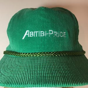 May include: Green corduroy baseball cap with a green rope band and the embroidered text "ABITIBI-PRICE" in white.