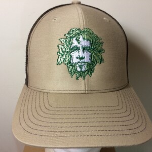 May include: A brown and tan trucker hat with a green and white embroidered image of a face with leaves. The face has a white beard and a white mustache.