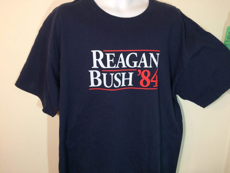May include: A navy blue t-shirt with the text "Reagan Bush '84" printed in white and red.