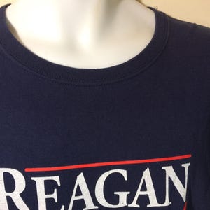 May include: A navy blue t-shirt with a white print that reads "REAGAN" in a red and white striped box.