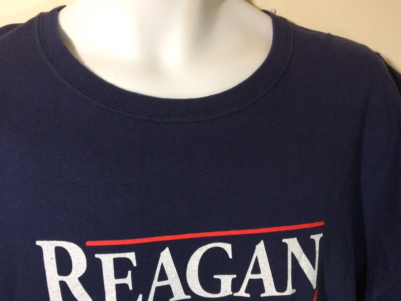 May include: A navy blue t-shirt with a white print that reads "REAGAN" in a red and white striped box.
