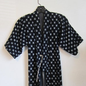 May include: A black and white patterned kimono with a white cord tie. The kimono has a square pattern.