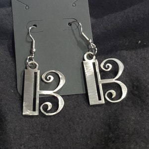 May include: A pair of silver earrings featuring a treble clef design. The earrings are made of metal and have a simple, elegant style.